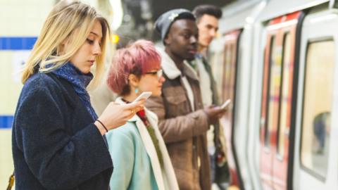 A woman looks at her phone on a tube platform in London