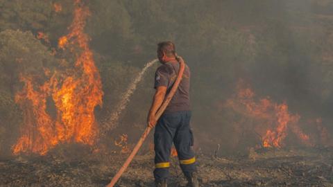 Firefighter Nektarios Kefalas tries to extinguish a wildfire burning near the village of Asklipieio, on Rhodes