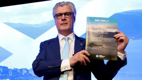 Malcolm Offord, Leader of Reform UK Scotland holds up a copy of the manifesto after delivering a speech at Ingliston Country Club and Hotel on March 19, 2026 in Bishopton, Scotland