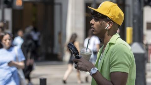 A man stands with an iced drink and a fan