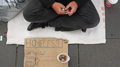 Hands, sign and money cup belonging to a homeless man