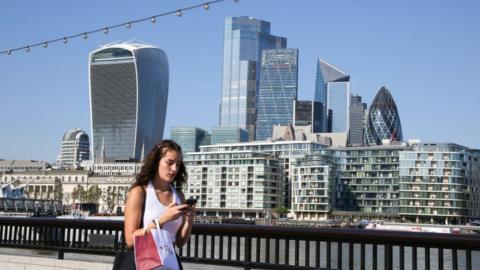 Woman using mobile phone in front of City of London skyline.
