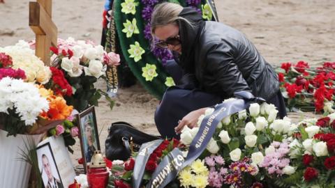 A woman lights a candle at the grave of Captain 3rd rank Vladimir Sukhinichev, one of the 14 crew members who died in a fire on a Russian navy"s deep-sea research submersible,