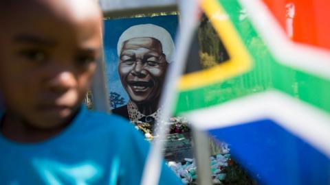 A boy plays with a South African national flag in front of a mural of Nelson Mandela in Soweto Township, as the funeral of former South African President takes place in Qunu, on December 15, 2013 in Soweto, South Africa