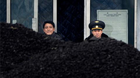 This file picture taken on 14 December 2012 from China's northeastern city of Dandong, looking across the border, shows a North Korean military officer (R) and a North Korea man (L) standing behind a pile of coal along the banks of the Yalu River in the northeast of the North Korean border town of Siniuju