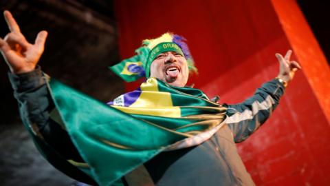 A man dressed in a Brazilian flag raises his arms in celebration