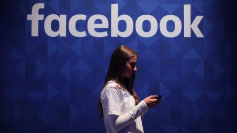 Woman using phone under a Facebook logo.