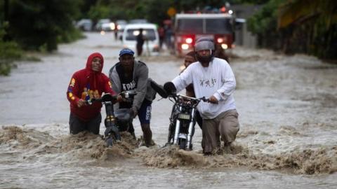 People cross a flooded road as a result of the intense rains, in San Jose de Ocoa, Dominican Republic 18 November 2023.