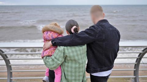 Amy and Peter with Rosie, in a photograph taken from behind, showing them looking out to sea