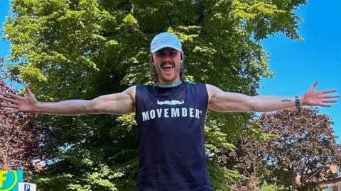 Harry Cleary in his running gear and Movember t-shirt with his arms outstretched