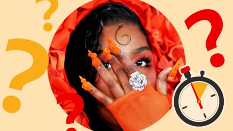 Lizzo wearing an orange head-dress, fingerless gloves and elaborate false nails, holding a hand with a huge metal ring in front of her face