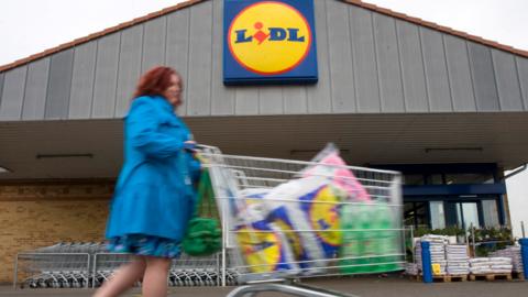 A woman with a trolley walking past a Lidl store