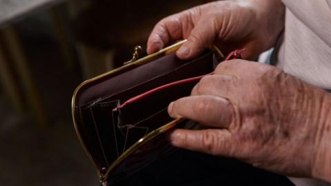 The hands of an elderly woman with an empty purse