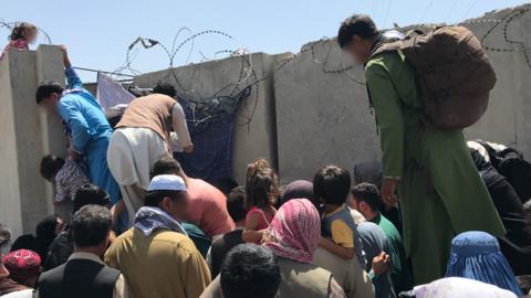People trying to climb a wall to Kabul airport in order to flee
