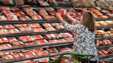 A woman looks at meat in a grocery store