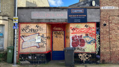 The closed shop with boarded-up windows, graffiti and a for-sale sign