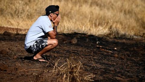 Maui resident John Rey Serrano reacts while looking from a road above Lahaina Town in the aftermath of a wildfire in Lahaina, western Maui, Hawaii on August 11, 2023
