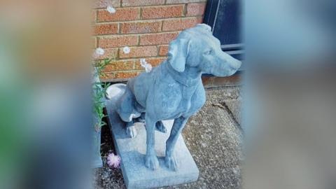 Light grey statue of a hunting dog standing on a plinth outside a house