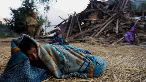 A boy sleeps on the floor next to a house collapsed during an earthquake in Jajarkot