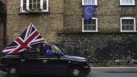 A black cab drives by an EU flag.