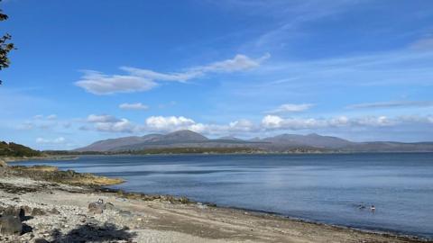 Partly cloudy coastal scene with hills in the background