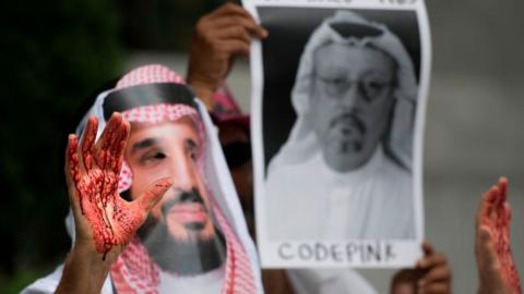 Protester dressed as MBS, with 'blood' on his hands, beside a picture of Khashoggi, in Washington on 8 December 2018