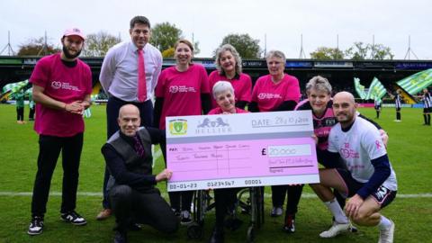 Massive cheque on the pitch with people in pink kits