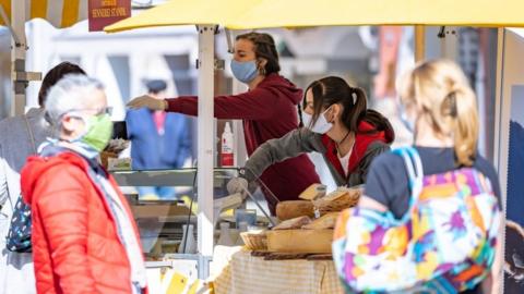 People wearing protective masks buy food at the city market in Lienz, Austria, on April 11, 2020