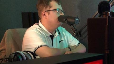 The Hub's broadcast room with a person sitting in front of a mic and a large 'ON AIR' light box in front of them