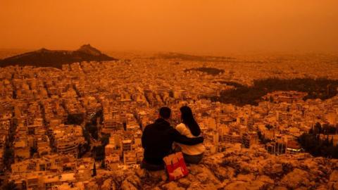 A couple sits on Tourkovounia hill, as southerly winds carry waves of Saharan dust, in Athens
