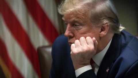 President Trump leaning on his hand with the American flag in the background