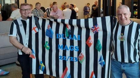 Neil Mitchell holding a banner saying Dubai Mags 22/23