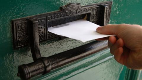 Hand putting letter through letterbox of a green door