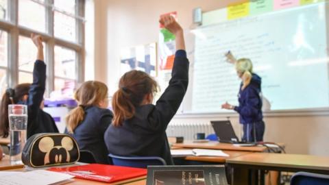 Students in a classroom with their hands up