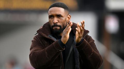 A photo of Jermain Defoe applauding in a brown jacket