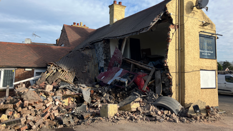 A damaged beige-coloured building with large chunks taken out of the sides and bricks exposed.