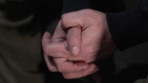 Close up of Adam's hands clasped together. Very little else can be seen, other than his black sleeves.