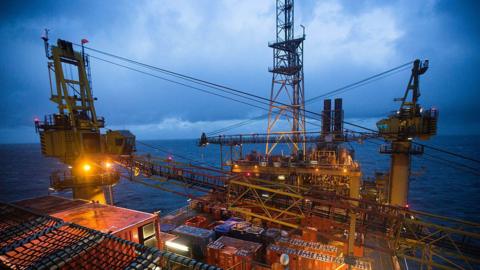 Offshore oil platform lit up by lights standing alone in the sea under a cloudy sky