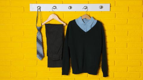 School uniform shirt, jumper, pants and tie hanging on yellow brick wall