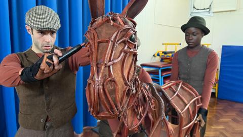 A War Horse puppet with puppeteers in a school hall