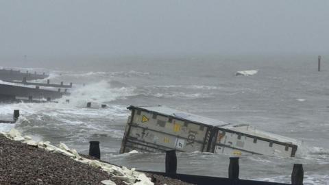 A shipping container washing up on a stony beach.