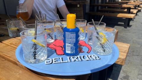 A blue tray with suncream and glasses of water on for customers to use. The tray is on a picnic bench in the beer garden of the Head of Steam pub in Sheffield city centre.