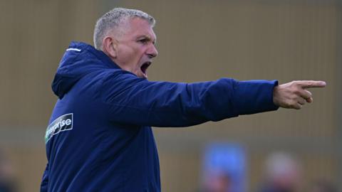 John Askey wearing a tracksuit and pointing with his finger while shouting