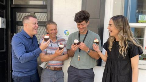 Sanctuary Trust staff at a fundraising initiative. The four staff are seen laughing together while holding cupcakes outside the Sanctuary Trust office.