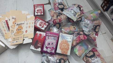 Flattened boxes and packages with pictures of fake Labubu dolls and the fake dolls are laid out on a table.