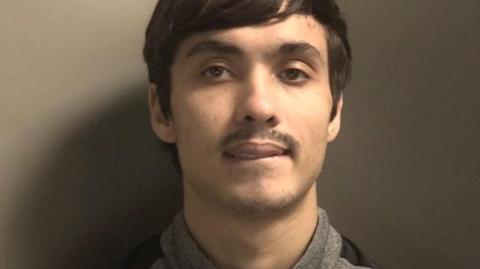 A police mugshot of James Byrne, a man in his early 20s with brown hair swept to the side and a moustache. 