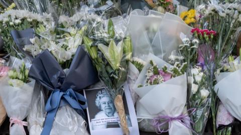 A photograph of Queen Elizabeth II surrounded by flower bouquets is seen outside the British Consulate