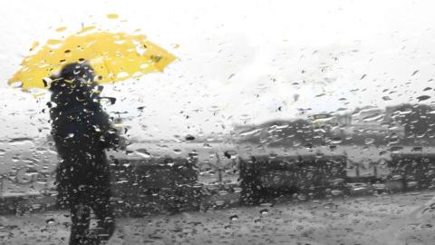 A person walking in the rain with a yellow umbrella up