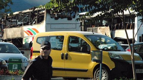 A policeman stands near buses destroyed in a bomb attack at Burgas airport, Bulgaria (18 July 2012)