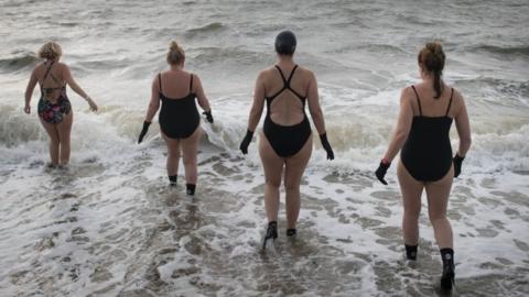 Four women walk into choppy sea waters